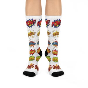 May include: White socks with comic book-style sound effects in red, yellow, blue, and green. The words "POW!", "SMACK!", "HAM!", "BANG!", "WHAT!", and "OMG!" are displayed on the socks. The heels and toes are black.