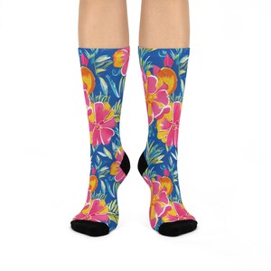 May include: Knee-high socks with a colourful floral design. The pattern includes large pink and yellow flowers, orange fruit, and green leaves on a bright blue backdrop. The socks have black heels and toes.