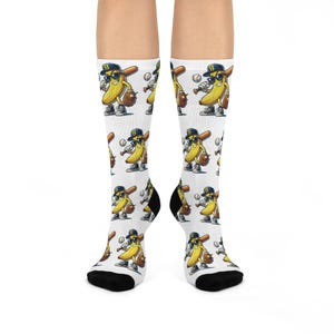 Könnte beinhalten: Weiße Socken mit einem sich wiederholenden Muster einer Cartoon-Banane, die eine Baseballkappe, eine Sonnenbrille und einen Baseballhandschuh trägt und einen Schläger hält. Die Banane hält auch einen Baseball. Die Socken haben schwarze Fersen und Zehen.