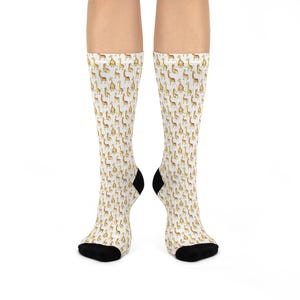 May include: A pair of knee-high socks with a repeating pattern of yellow giraffes on a white background. The socks have black heels and toes. The giraffe design features a simple, cartoon-like style.