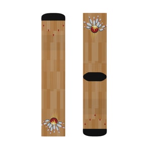 May include: A pair of socks featuring a bowling theme. The socks have a brown wooden floor pattern with a black heel and toe. A bowling ball with flames and pins are printed on the socks.