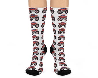 Puede incluir: Calcetines blancos con un patrón repetido de monster trucks rojos. Los camiones tienen neumáticos negros y ventanas azules. Los calcetines tienen talones y dedos negros.