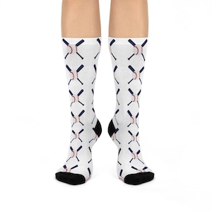 Può includere: Calzini bianchi con un motivo ripetuto di mazze da baseball incrociate e palle da baseball. Le mazze sono blu navy e le palle da baseball sono rosse con cuciture bianche.