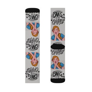 May include: A pair of novelty socks with a light gray background and black accents. The socks feature a pop art style illustration of a woman with a surprised expression, along with the text "OMG NO ONE CARES".