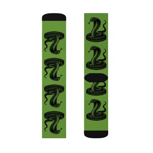 Puede incluir: Un par de calcetines verdes con un gráfico de serpiente cobra negra repetido en los calcetines. Los calcetines son de longitud media.