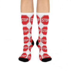 May include: White socks with a repeating pattern of red stop signs. Each stop sign has the word "STOP" in white letters. The socks have black heels and toes.