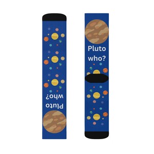 Può includere: Un paio di calzini blu a tema spaziale. Un calzino presenta il testo "Pluto who?" e una grafica del pianeta. L'altro calzino ha la stessa grafica del pianeta e il testo "who? Plutone". I calzini hanno polsino e punta neri.