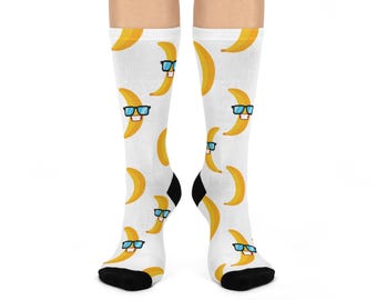 May include: White socks with a repeating pattern of yellow bananas wearing blue sunglasses. The socks have black heels and toes. The bananas have smiling faces.