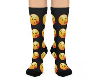 May include: Black knee-high socks featuring a repeating pattern of yellow emoji faces blowing kisses, each with a red heart. The socks have a black toe and heel.