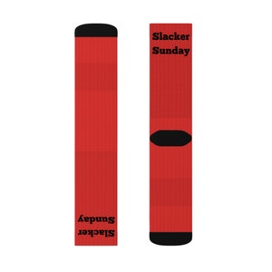 May include: Pair of red socks with black heels and toes. The text "Slacker Sunday" is printed in black on both socks. The socks are made of a ribbed knit material.
