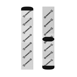 May include: A pair of crew socks with a repeating pattern of gray wrenches on a light gray background with vertical stripes. The toe and heel are black. The wrenches are in a diagonal pattern.