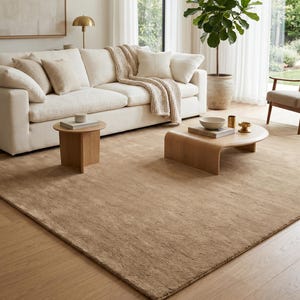 Modern beige hand tufted wool rug displayed in a bright minimalist living room featuring a curved cream sofa, accent chairs, walnut coffee table, warm oak flooring, and natural sunlight. The luxurious sand beige area rug showcases a dense plush pile and elegant solid color design that creates warmth, softness, and timeless sophistication. Handmade from premium New Zealand wool, this custom area rug is perfect for modern living rooms, Scandinavian homes, Japandi interiors, luxury apartments,