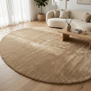 Modern beige hand tufted rug displayed in a designer-inspired living room featuring oversized sectional seating, natural wood coffee tables, soft textiles, indoor plants, and abundant natural lighting. The plush wool surface introduces subtle texture and visual warmth while the neutral sand beige palette complements Scandinavian, Japandi, contemporary, organic modern, and luxury interior styles with effortless elegance.