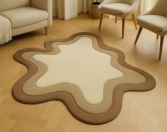 Puede incluir: Una alfombra única y en capas con una forma irregular. La alfombra presenta un degradado de color, que va desde un centro beige claro hasta capas exteriores marrón medio y oscuro. La alfombra está colocada sobre un suelo de parquet marrón claro.