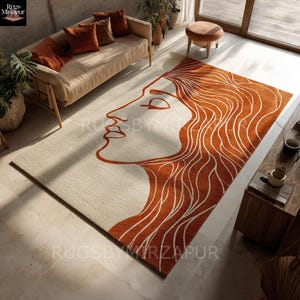 May include: A rectangular area rug featuring a minimalist design of a woman's profile in burnt orange against a cream background. The rug's design includes flowing hair and facial features. The rug is placed in a living room setting.