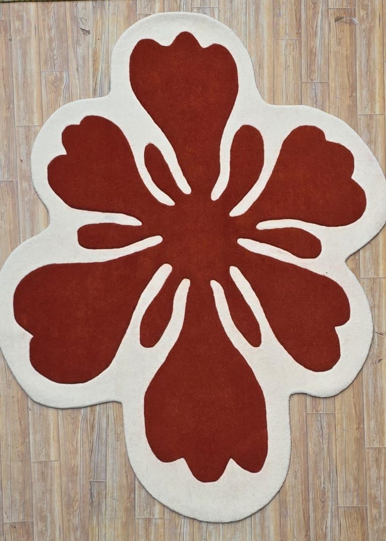 May include: A large, flower-shaped rug with a bold design. The rug features a deep red center with white petal outlines. The rug is placed on a light-colored wooden floor, creating a striking contrast.