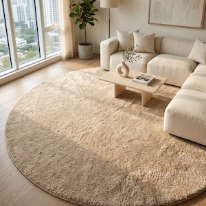 Luxury handmade wool rug in an elegant sand beige shade styled beneath contemporary furniture in a bright residential living room. The dense plush surface beautifully reflects natural light, creating soft tonal variations and inviting warmth throughout the interior. Crafted from premium New Zealand wool, this timeless area rug enhances modern homes, luxury apartments, boutique interiors, and designer projects with superior craftsmanship and refined simplicity.