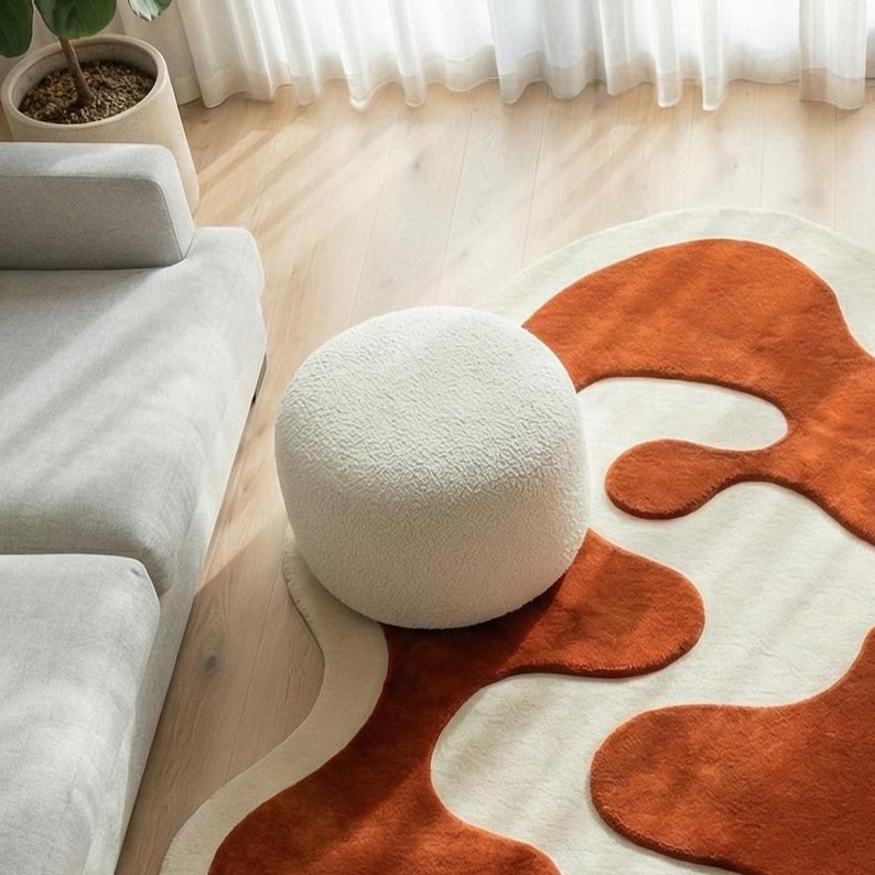 Luxury handmade wool rug featuring bold terracotta abstract motifs carved in high-low relief against a warm ivory base. Crafted using traditional tufting techniques, this sculptural rug offers a soft underfoot feel and artistic texture. Shown in a bright modern interior with neutral furniture, highlighting the rug as a statement centerpiece.