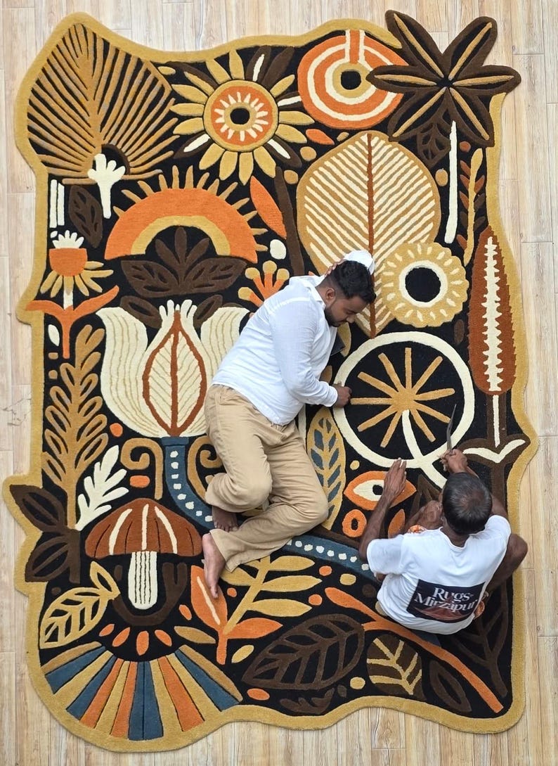 Hand-tufted wool wall rug featuring folk botanical artwork with flowers, leaves, mushrooms, and sun motifs in warm earthy colors, displayed above a modern sofa.