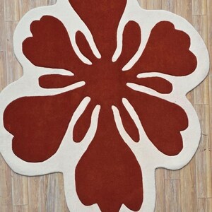 May include: A large, flower-shaped rug with a bold design. The rug features a vibrant red center with white petal outlines, creating a striking contrast. The rug's unique shape and color scheme make it a statement piece for any room.