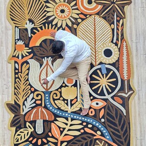 Wool wall rug artwork with folk floral design, blending earthy tones and organic shapes for a cozy modern aesthetic.