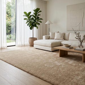 Luxury beige round wool rug positioned beneath contemporary curved seating in a bright designer living room with neutral furniture, warm wood flooring, soft daylight, and sophisticated décor. This hand tufted area rug features a plush velvety surface and calming sand beige color that complements Scandinavian, organic modern, minimalist, coastal, and luxury interiors. Handmade from premium wool, this custom rug creates an inviting atmosphere while providing comfort, durability