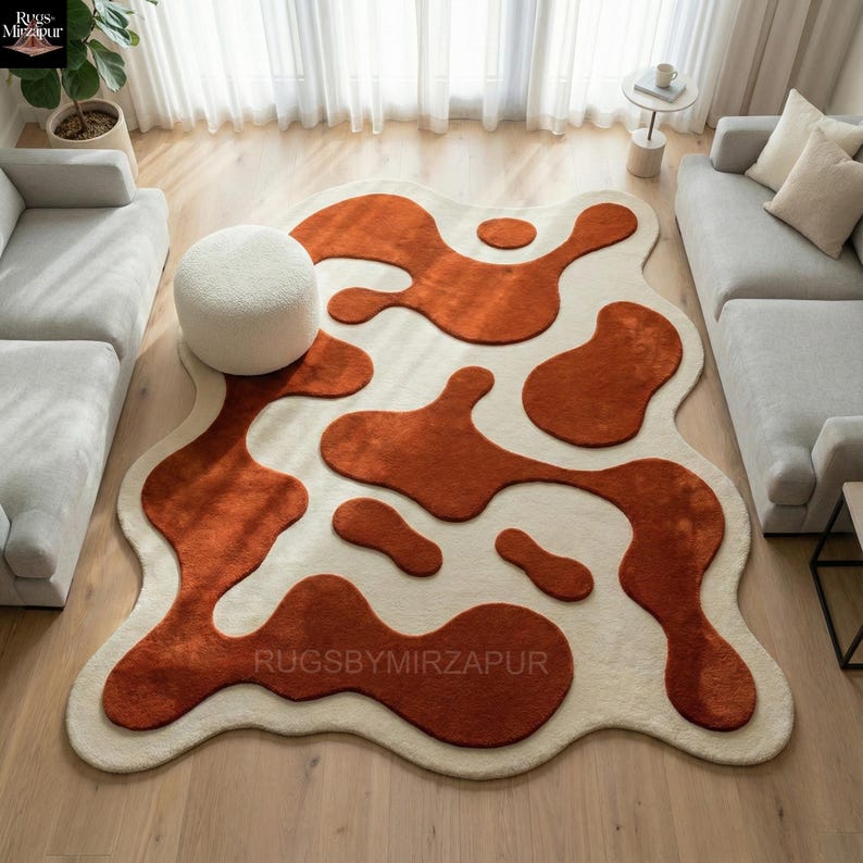 Hand tufted abstract wool rug with organic freeform shape, featuring raised terracotta and rust-colored motifs on a soft ivory base. The rug showcases a high-low carved pile creating sculptural depth and texture. Styled in a modern living room with neutral sofas, wooden flooring, and natural daylight, this artisan rug adds warmth, movement, and contemporary artistic appeal to the interior.