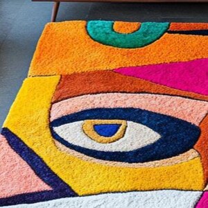Colorful abstract hand-tufted wool rug inspired by cubist art, created by Rugs By Mirzapur. With bold geometric shapes and expressive eyes, this unique design transforms any living room into a modern art space. The soft wool pile provides warmth and comfort, while vibrant hues bring artistic life to contemporary décor.