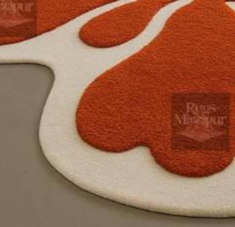 Abstract retro amoeba rug with bold orange and white design placed under white sectional sofa.