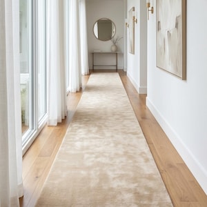 Premium sand beige hand tufted wool rug styled in a contemporary living room featuring oversized sectional seating, indoor fiddle leaf fig tree, modern coffee table, floor-to-ceiling windows, and abundant natural light. The plush wool construction creates exceptional softness underfoot while the neutral beige tone brightens the room and enhances spaciousness. Handmade craftsmanship and premium New Zealand wool make this rug perfect for luxury homes, designer apartments