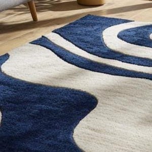 Navy blue and ivory abstract wave rug from Rugs By Mirzapur, handcrafted with soft wool. The modern curved design adds motion and serenity to interiors. Ideal for living rooms and studios, this high-quality rug blends artistic beauty with long-lasting durability and comfort.