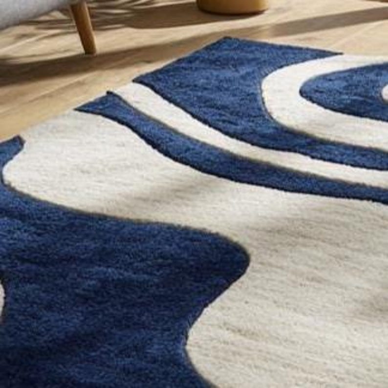 Navy blue and ivory abstract wave rug from Rugs By Mirzapur, handcrafted with soft wool. The modern curved design adds motion and serenity to interiors. Ideal for living rooms and studios, this high-quality rug blends artistic beauty with long-lasting durability and comfort.
