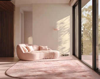 May include: A blush pink rug and curved sofa set in a modern living room. The rug has a soft, watercolor-like design. The sofa is upholstered in a matching pink fabric and has three throw pillows. The room has large windows and a minimalist design.