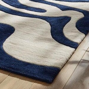 Handmade wool rug with navy and ivory abstract pattern, designed by Rugs By Mirzapur. The modern wave design enhances any living room or bedroom décor. Soft, durable, and elegant, this rug embodies artistry, craftsmanship, and a sense of calm movement.