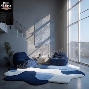 Könnte beinhalten: Moderne Wohnzimmereinrichtung mit einem großen, abstrakt geformten Teppich in Blau- und Weißtönen. Zwei weiche, marineblaue Sitzsäcke und ein kleiner Holztisch ergänzen die Szene. Der Raum hat ein minimalistisches Design mit einer Treppe und großen Fenstern.