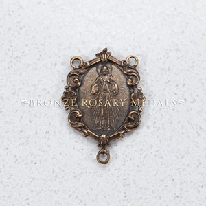 The Divine Mercy bronze center is surrounded by scrolls and flowers.  It is 1 3/8 inches tall a depicts Jesus displaying his Sacred heart.  This image is watermarked