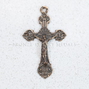 May include: A bronze crucifix with a detailed design. The crucifix features a figure of Jesus Christ on the cross. The cross has a decorative design with intricate details.