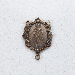The Divine Mercy bronze center is surrounded by scrolls and flowers.  It is 1 3/8 inches tall a depicts Jesus displaying his Sacred heart.