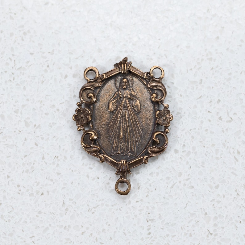 The Divine Mercy bronze center is surrounded by scrolls and flowers.  It is 1 3/8 inches tall a depicts Jesus displaying his Sacred heart.