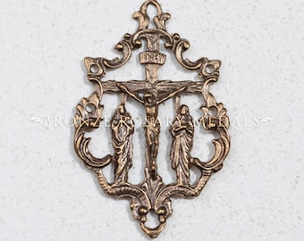May include: A gold-toned metal crucifix with a decorative frame and three figures. The figures are of Jesus on the cross and two other figures standing on either side of the cross. The cross has the inscription "INRI" above Jesus's head.