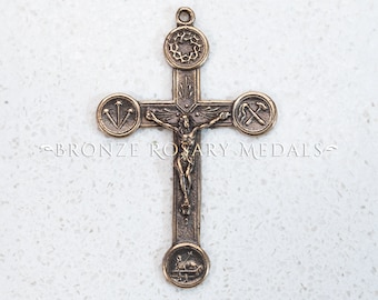 May include: A bronze rosary crucifix with a depiction of Jesus Christ on the cross. The crucifix has four medallions with religious symbols, including a crown of thorns, nails, a hammer, and a lamb.