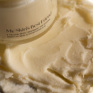 May include: A white jar of skin balm with the text "My Skin's Best Friend" and "A Tallow Spot Treatment for Eczema, Sensitive Skin, & Everything Else" on the label. The balm is spread out on a white surface.