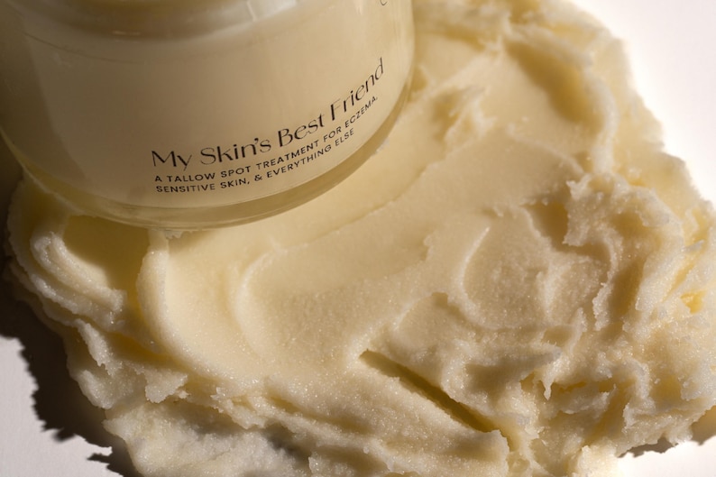 May include: A white jar of skin balm with the text "My Skin's Best Friend" and "A Tallow Spot Treatment for Eczema, Sensitive Skin, & Everything Else" on the label. The balm is spread out on a white surface.