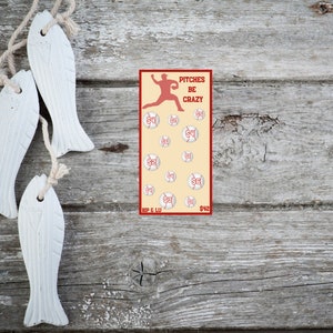 May include: A red and white baseball themed game card with the text "Pitches Be Crazy" and a silhouette of a baseball player. The card has 12 baseballs with numbers on them. The card also has the text "Kip & Lu" and "$42".