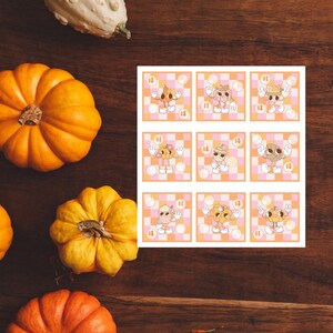 May include: Nine printable cards featuring a cartoon pumpkin character in different poses. Each card has a checkered background with pink and white squares. The pumpkin character is wearing a hat and holding a number of pumpkins.