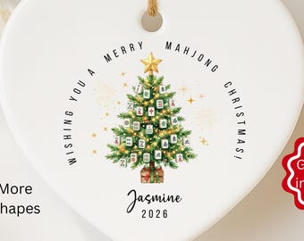 May include: A heart-shaped white ceramic Christmas ornament with a Mahjong Christmas tree design. The ornament has a gold star on top and the text "Wishing You a Merry Mahjong Christmas!" around the tree. The name "Jasmine" and the year "2026" are also printed on the ornament.