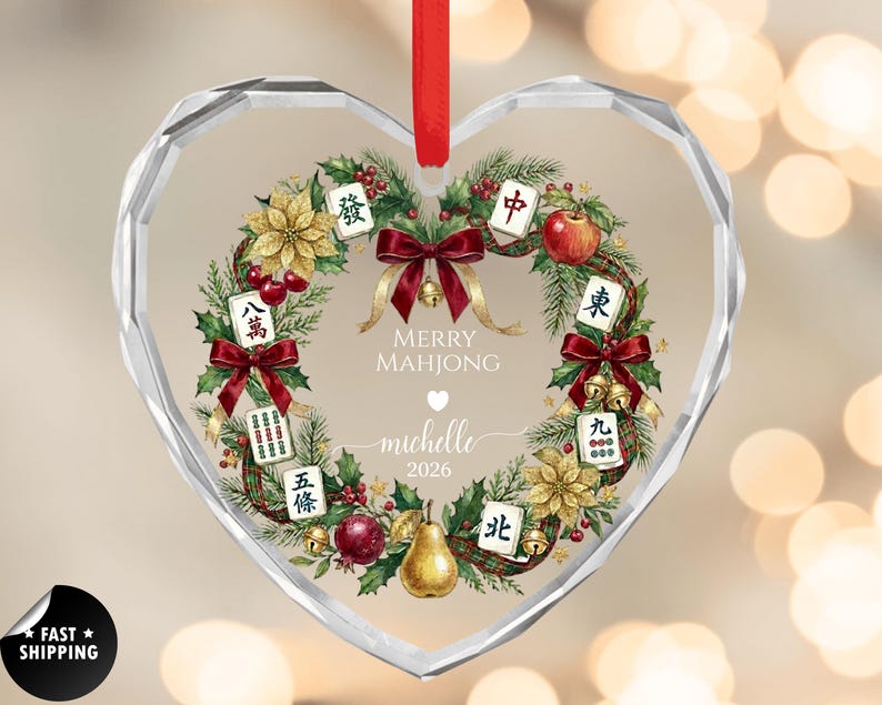 May include: Heart-shaped glass ornament with a festive Mahjong-themed design. The ornament features a wreath of greenery, red bows, and Mahjong tiles. The text "MERRY MAHJONG" and a name and year are printed in the center.