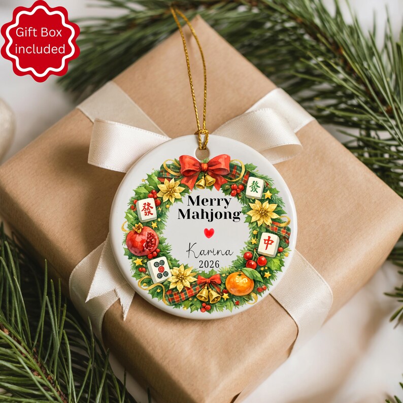 Pu&ograve; includere: Ornamento natalizio in ceramica bianca con un filo dorato, con un design a ghirlanda con la scritta "Merry Mahjong" e il nome "Karina" con l'anno 2026. La ghirlanda include fiocchi rossi, fiori e tessere di Mahjong. L'ornamento &egrave; su un regalo confezionato.