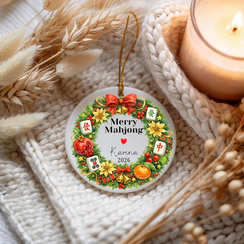 Pu&ograve; includere: Un ornamento natalizio rotondo con un design a ghirlanda festiva. La ghirlanda include fiocchi rossi, fiori gialli e illustrazioni di tessere di Mahjong e un melograno. L'ornamento presenta il testo "Merry Mahjong" e il nome "Karina" con l'anno "2026".