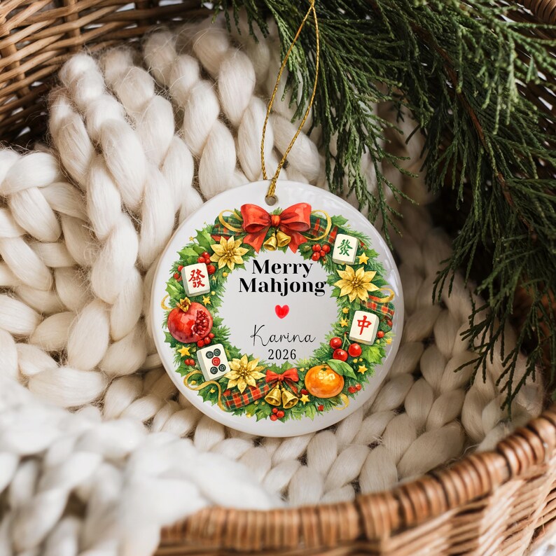 Pu&ograve; includere: Ornamento natalizio rotondo in ceramica con un cordino dorato. Presenta un design a ghirlanda con le parole "Merry Mahjong", il nome "Karina" e l'anno "2026". La ghirlanda include un fiocco rosso, fiori e tessere di Mahjong.